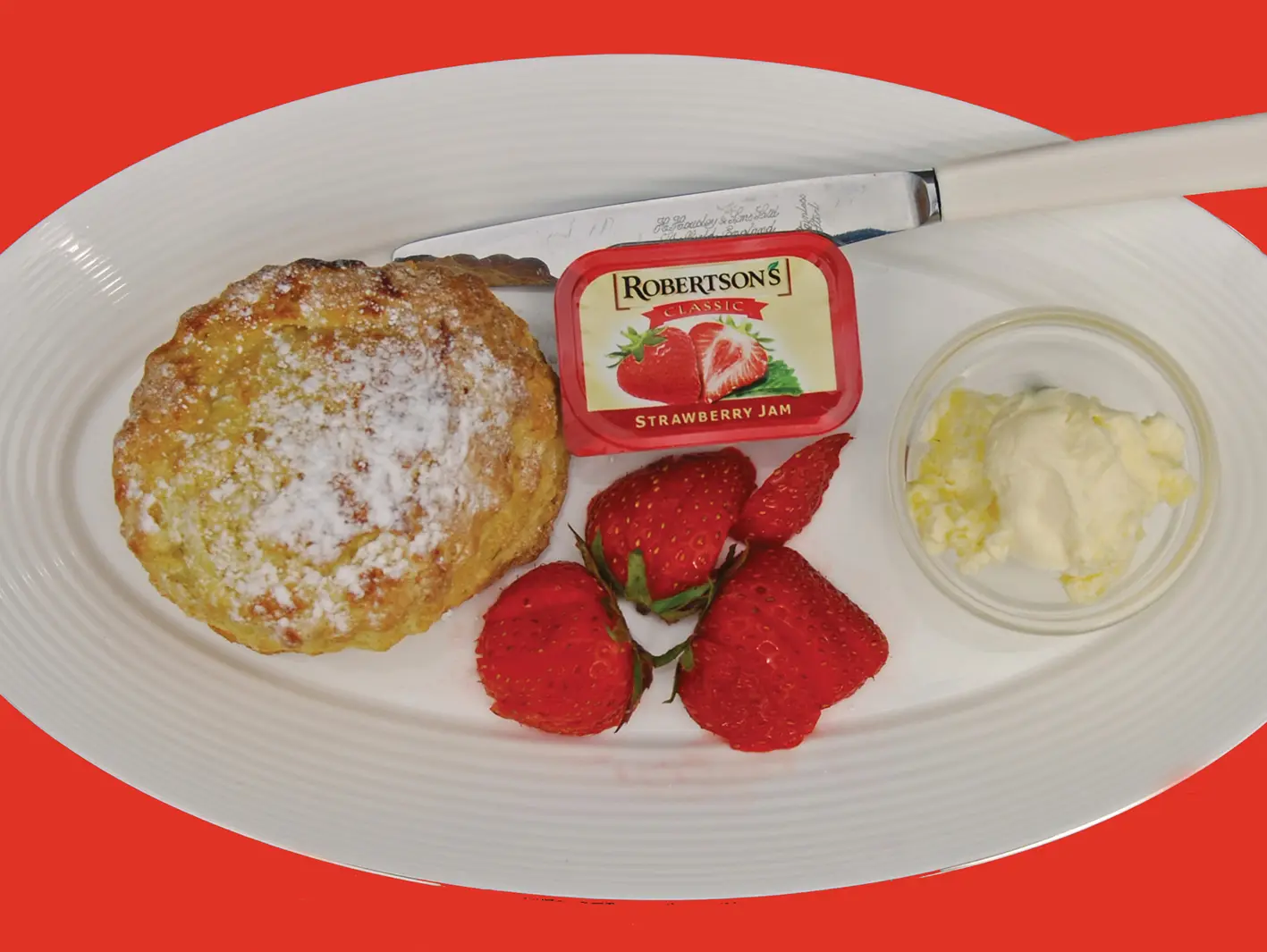 A freshly baked scone with strawberry jam, clotted cream and a cup of tea